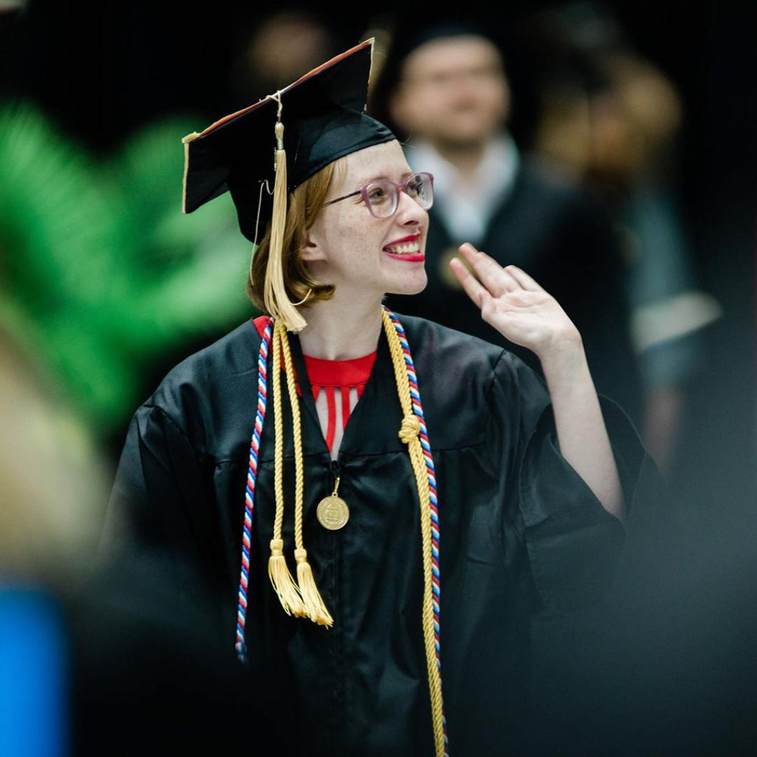 Photo of Sadie walking at graduation; she's waving at the crowd